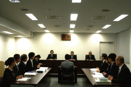 不利益処分についての不服申立てにおける口頭審理において、公平委員会(正面)、請求者側(左)、処分者側(右)が出席し、証人尋問を行っている様子(模擬審理)。